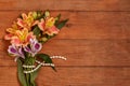 A small bouquet of Alstroemeria with a pearl thread on wooden brown background