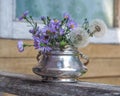 A small bouquet of blue New Belgian asters and fluffy dandelions in a metal sugar bowl Royalty Free Stock Photo