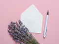 Small bouquet of fragrant blooming lavender on a white paper envelope and white ballpoint pen over a textural pink background.