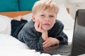 Small boy laying on his bed looking at his laptop