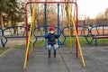 A small boy in a medical mask sits on a swing in the spring. The concept of protection against coronavirus infections covid-19