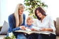 A small boy with mother and grandmother looking at photos at home at Christmas time. Royalty Free Stock Photo