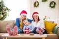 A small boy with mother and grandmother with Santa hat at home at Christmas time. Royalty Free Stock Photo
