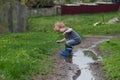 a small boy in rubber boots jumps through a muddy puddle