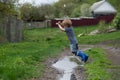 a small boy in rubber boots jumps through a muddy puddle