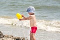 A small boy on the seashore pours water from a bucket against the background of the sea and waves, Royalty Free Stock Photo