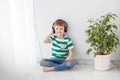 A small boy is sitting on the floor in a bright room listening to music with headphones Royalty Free Stock Photo