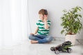 A small boy is sitting on the floor in a bright room listening to music with headphones, next to a toy car Royalty Free Stock Photo