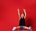 Small boy in stylish casual clothing, hair bandana and white sneakers sitting on floor and feeling excited with hands raised up