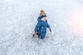 A small boy of 4-6 years old, kneeling, skating, in the winter in the city on an ice rink. Happy smiling, trying to ride Royalty Free Stock Photo