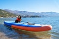 small brave dog dachshund in orange life jacket and sunglasses is surfing on a SUP board on the sea. Live Guard and Royalty Free Stock Photo