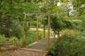 A small bridge with a wooden archway crosses a small stream in a quiet English garden