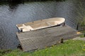 a small bright empty old rowing boat is moored to the wooden pier on a small river Royalty Free Stock Photo