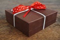 Small brown gift box wrapped with white ribbon and red dotted bow on the wooden background as a symbol of giving and getting Royalty Free Stock Photo