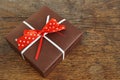 Small brown gift box wrapped with white ribbon and red dotted bow on the wooden background as a symbol of giving and getting Royalty Free Stock Photo