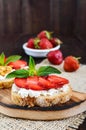 A small bruschetta with curd and fresh strawberries on a dark wooden background.