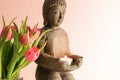 Small buddha sculpture made from ceramic with a burning candle and pink tulips against a light background with copy space, Royalty Free Stock Photo