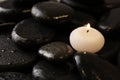 Small burning candle on beautiful wet spa stones