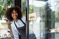 Small business african female owner smiling while turning sign for opening of cafe. Happy afro-american waitress Royalty Free Stock Photo
