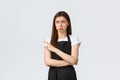 Small business, employees and coffee shop concept. Jealous and upset cute barista in black apron pouting unsatisfied and