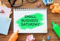 Small business Saturday highlighted in green colour on a notepad lying on wooden surface together with colourful markers, crumpled