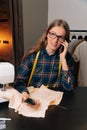 Small business sewing clothes, home atelier stylish sewing in glasses receiving order on a smartphone