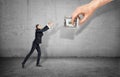 Small businessman on concrete background reaching out for a giant hand holding money. Royalty Free Stock Photo