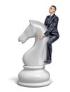 A small businessman rides a giant white chess knight figure as a horse.