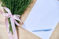 Small camomiles bouquet tied with pink ribbon and white paper sheet with light blue pen on wooden table. Natural background with Royalty Free Stock Photo