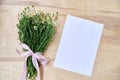 Small camomiles bouquet tied with pink ribbon and white paper sheet on wooden table. Natural background picture of wild flowers. Royalty Free Stock Photo