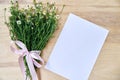 Small camomiles bouquet tied with pink ribbon and white paper sheet on wooden table. Natural background picture of wild flowers. Royalty Free Stock Photo