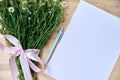 Small camomiles bouquet tied with pink ribbon and white paper sheet on wooden table. Natural background picture of wild flowers. Royalty Free Stock Photo