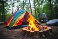 small campfire burning in front of a colorful tent