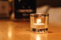 A small candle burns in a glass on a wooden table