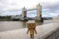 A small cardboard toy stands on the background of the old bridge