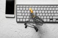 Small cart with computer keyboard and mobile phone on white background. Online shopping Royalty Free Stock Photo