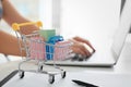 Small cart on table of woman using laptop. Internet shopping concept Royalty Free Stock Photo