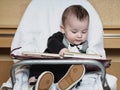 Small caucasian baby boy sitting in chear with notepad