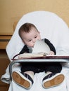 Small caucasian baby boy sitting in chear with notepad