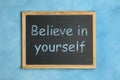 Small chalkboard with motivational quote Believe in yourself on light blue background, top view