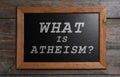 Small chalkboard with phrase What Is Atheism? on wooden background