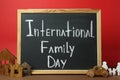 Small chalkboard with text International Family Day, wooden house models, people figure and toy car on brown table against red Royalty Free Stock Photo