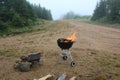 A small charcoal barbecue with fire coming from it on a foggy day in summertime.