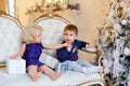 Small charming baby boy in a blue sweater and a little blond girl sitting in a chair against a background of Christmas lights and Royalty Free Stock Photo