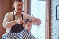 Small charming boy is getting trendy haircut from expirienced barber at fashionable hairdressing salon