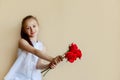 Small charming schoolgirl pereds bouquet of red flowers. on beige background.