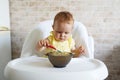 A small, cheerful, charming girl trying eat yogurt herself