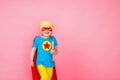 Small cheerful child playing a superhero with a red Cape and a star, with a book