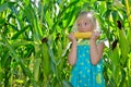 A small, cheerful girl in the green field eating corn