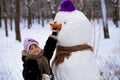 A small cheerful girl holds a big carrot, the nose of a big snowman Royalty Free Stock Photo